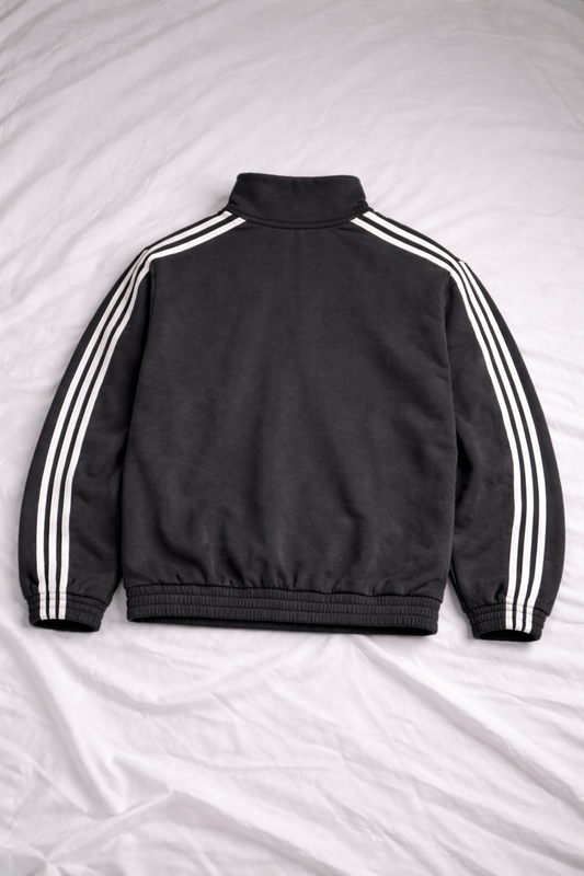 Black jacket with white stripes on sleeves and back, laid flat on a light gray surface.