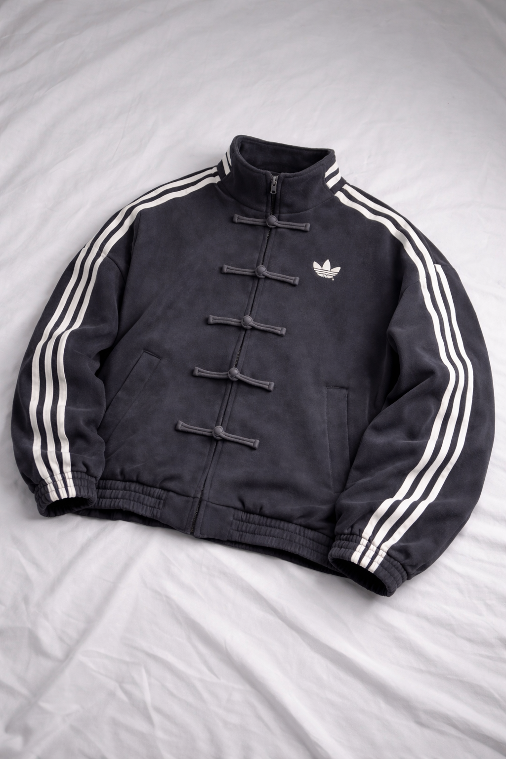 Black Adidas jacket with white stripes on a gray background