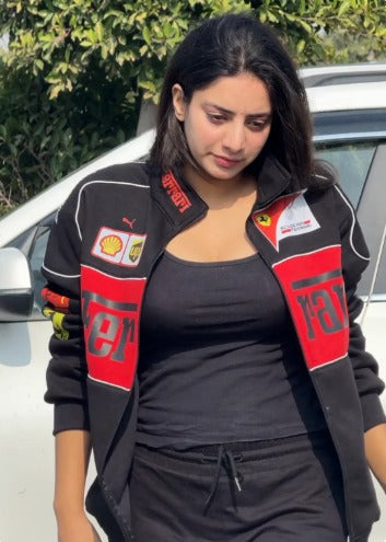Woman wearing a black and red jacket with logos, standing outdoors.