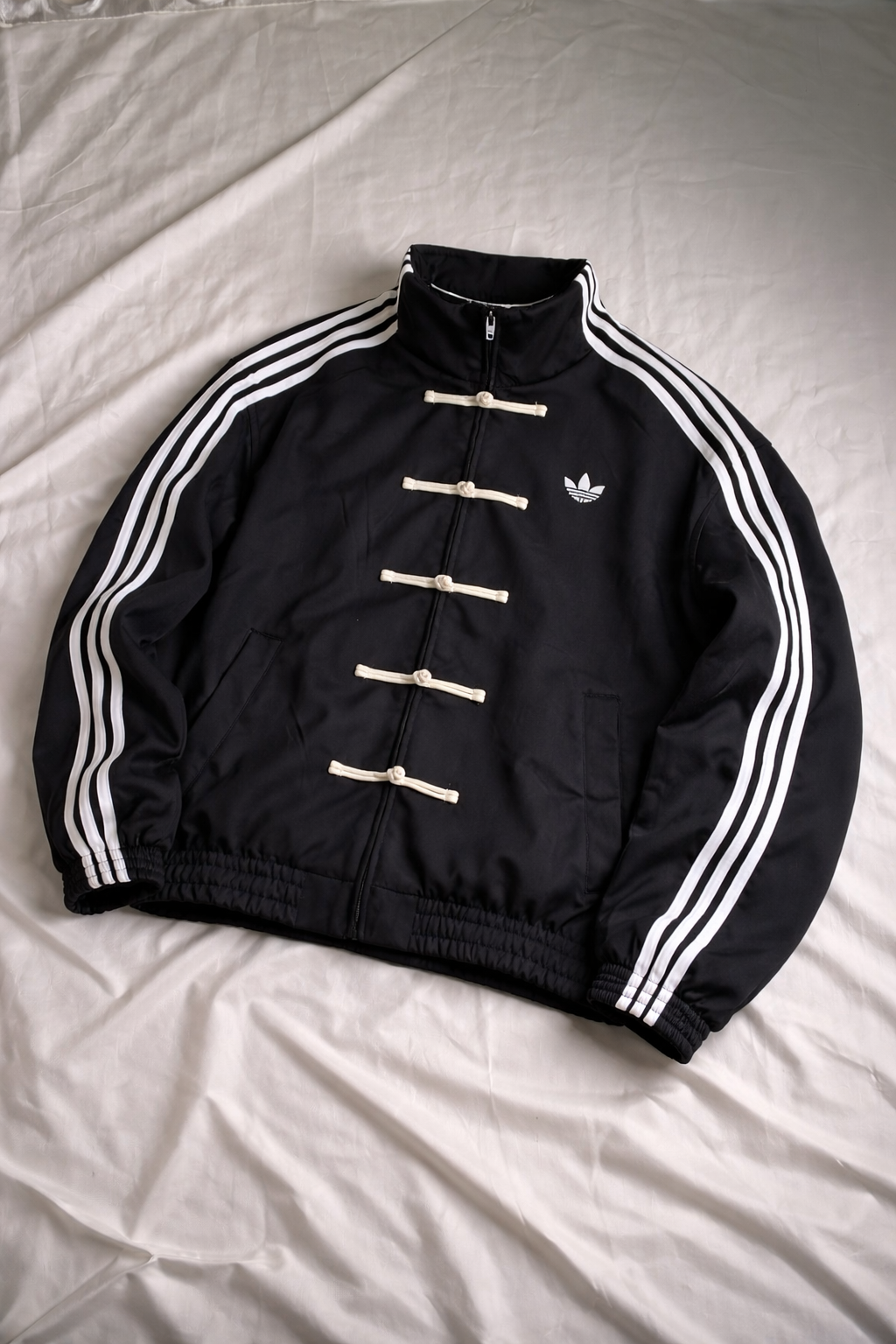 Black Adidas jacket with white stripes on a light gray background