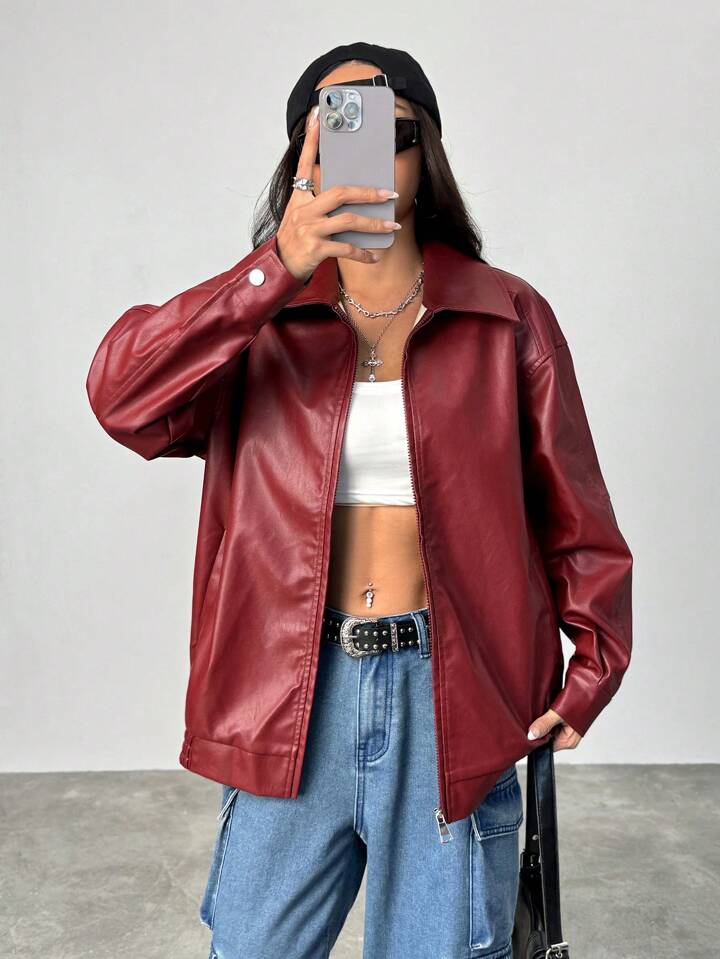 Person wearing a red leather jacket and blue jeans, taking a mirror selfie.