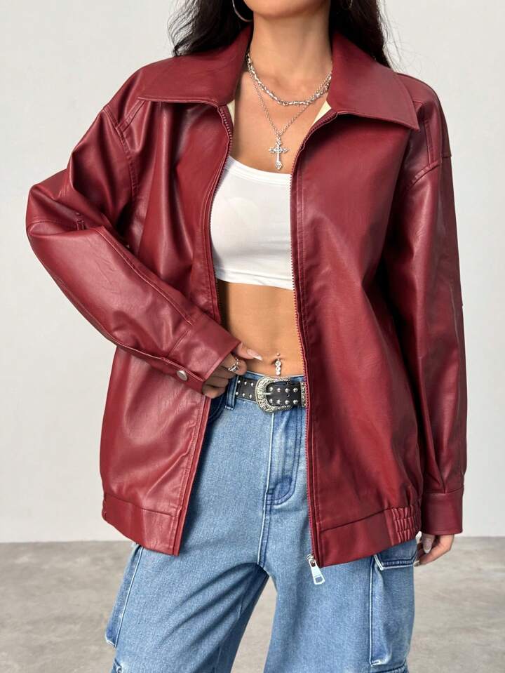 Person wearing a red leather jacket, white crop top, and blue jeans on a plain background