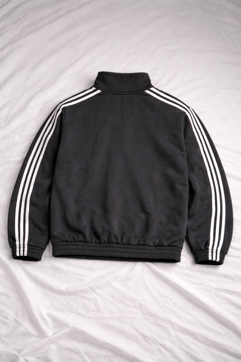 Black jacket with white stripes on sleeves and back, laid flat on a light gray surface.